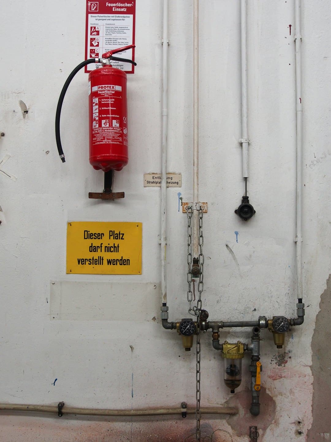 Ein roter Feuerlöscher und industrielle Warnschilder an einer Wand.